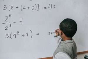 Kid doing sums on a whiteboard.