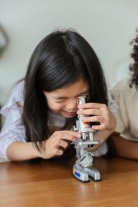 A young girl looks into a microscope during her science experiment.