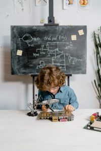 A child holds a magnifying class while closely looking at a circuit board.